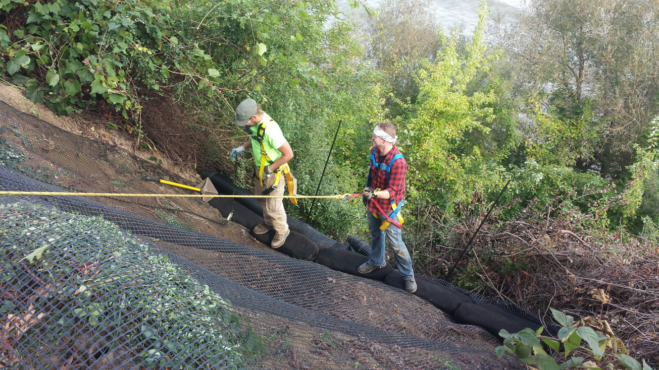 Two workers installing stabilization blocks on a steep incline